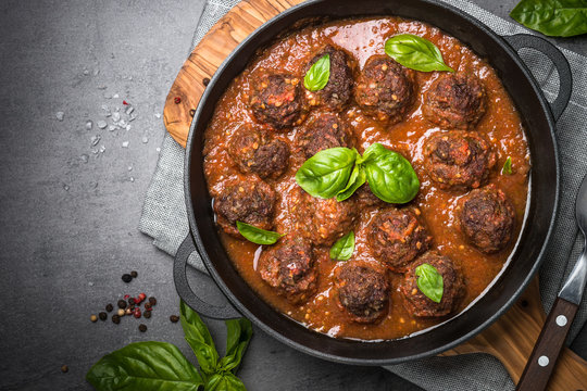 Meatballs in tomato sauce on a black slate background.
