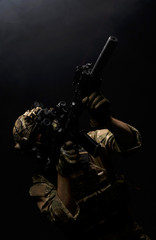 Soldier in military uniform with assault rifle aiming with laser at target in smoke on background of dark wall 18