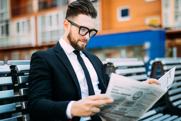Handsome businessman reading a financial newspaper while sitting on bench outdoors