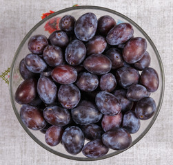 Plums in a glass dish on a linen fabric.