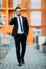 Handsome bearded businessman in classic suit is using a smart phone while standing on the balcony of the office