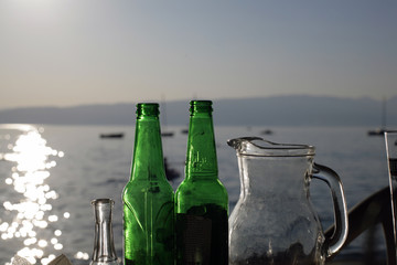 Close up empty bottles of beer and glasses on the beach sunset; drinks and summer concept.
