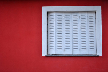 Fototapeta na wymiar Closed white window on a red colored facade.