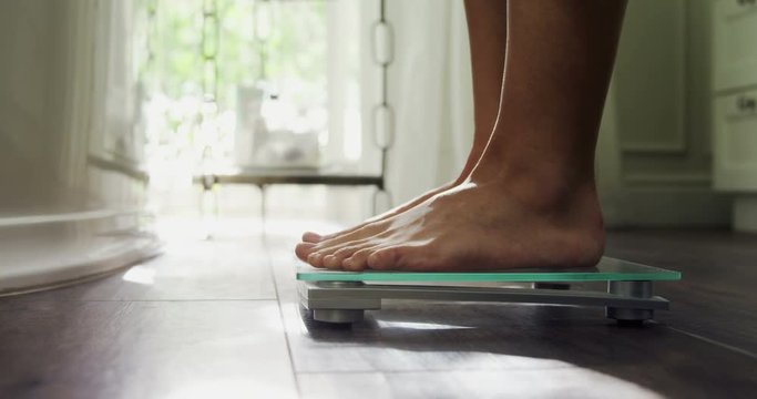 Woman checking her weight on weighing scale at home 