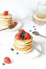 Pancakes with berries and honey on white background