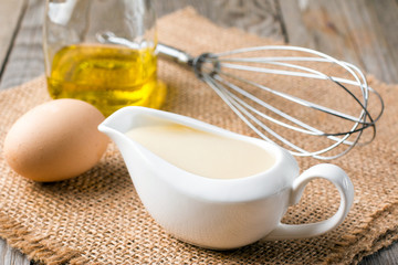 Fresh homemade white sauce Mayonnaise and ingredients eggs, lemon olive oil on wooden background