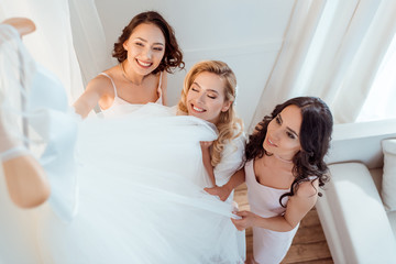 bride with bridesmaids touching wedding dress