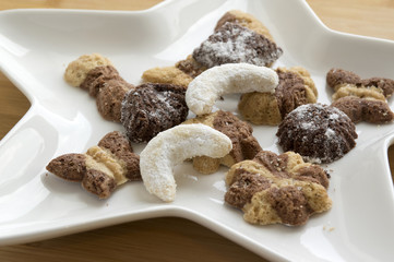 Many kinds of Christmas cookies on white plate, gingerbread dark and light, star shape dish, bamboo wooden background