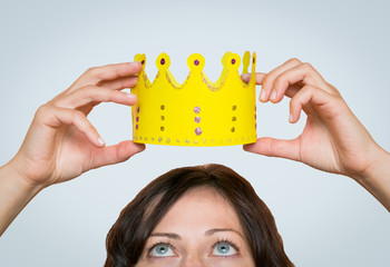 Beautiful young woman putting a paper crown on her head on the light grey background.