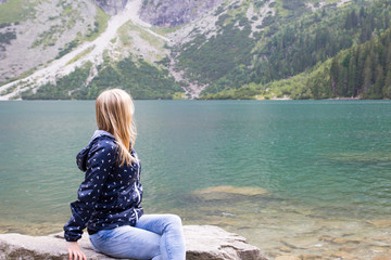 Blonde girl is sitting and watching the lake in the mountains