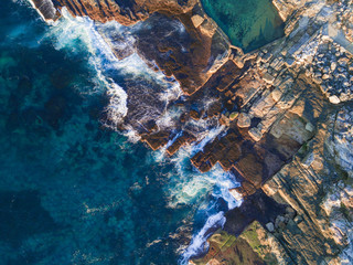 Look down view of rock cliff with clear sea water.