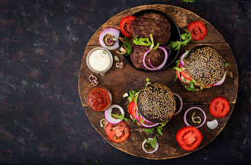 Black big sandwich -  black hamburger with juicy beef burger, cheese, tomato,  and red onion on black background