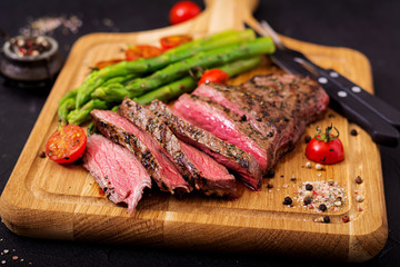 Juicy steak rare beef with spices on a wooden board and garnish of asparagus.