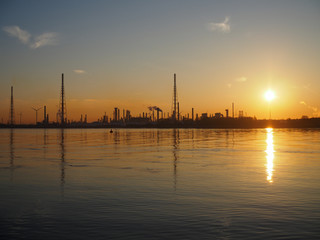 The silhouette of an oiil refinery near the water during sunrise.