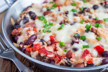 Baked rice casserole with black beans, pinto beans, kidney beans, cheese and paprika, in metal baking dish, horizontal