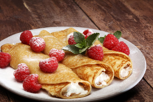 Homemade crepes served with fresh raspberrries and powdered sugar on rustic wooden table
