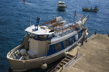 Piccola nave bianca ancorata alla banchina. Si tratta di un peschereccio adibito appunto alla pesca in mare. Dietro altre piccole barche si avvicinano al golfo.