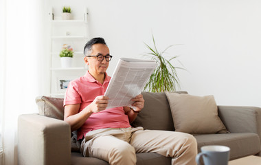 asian man in glasses reading newspaper at home