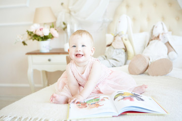 laughing little baby girl flipping a book on the bed