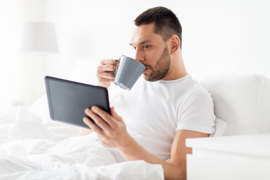 Man With Tablet Pc Drinking Coffee In Bed At Home