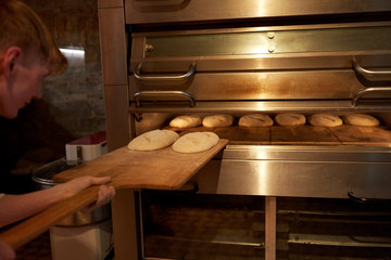 baker putting dough into bread oven at bakery