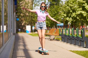 happy teenage girl in shades riding on longboard