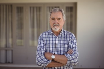 Senior man standing with arms crossed at home