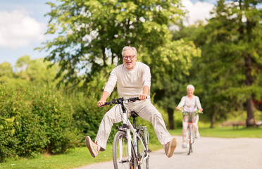 happy senior couple riding bicycles at summer park - obrazy, fototapety, plakaty