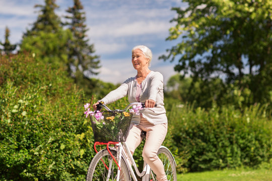 happy senior woman riding bicycle at summer park