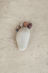 Group of pebble stones on sand creating de form of a foot in isolated white background