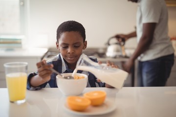 Fototapeta na wymiar Boy pouring milk into breakfast cereals bowl in kitchen