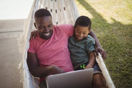 Father and son using laptop while relaxing on hammock