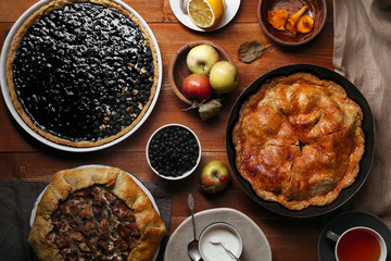 Traditional autumn pies arranged on red wooden rustic table. Chanterelle mushrooms, blueberry and sweet apple fillings. Top view.