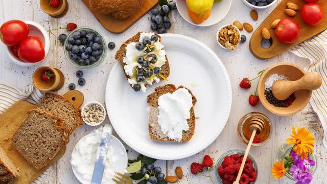 Making sandwiches with homemade bread, ricotta cheese, honey and various fresh fruits: blueberry, raspberry, apricot. Proposing healthy eating. Stop motion animation, top view