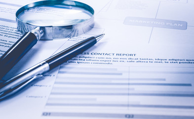 Business analysis concept. Magnifying glass and pen on documents marketing paper.
