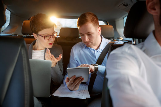 businesspeople with computer and tablet in car on trip.