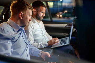 Businesspeople work on late night in back seat of car.