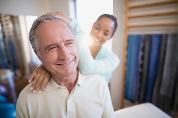 Smiling senior male patient receiving neck massage from female