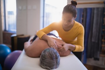 Shirtless male patient lying on bed receiving neck massage from