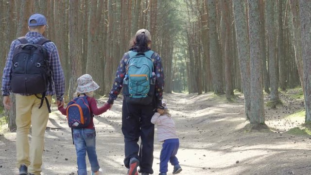 Sports family travels through  forest. A young mother and father of a tourist with a backpack leading her children through a forest road. Family travel together, hiking outdoors on nature.