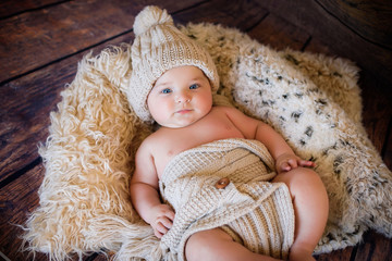 likable and pretty newborn baby boy with big blue eyes in a knitted hat on a wooden background