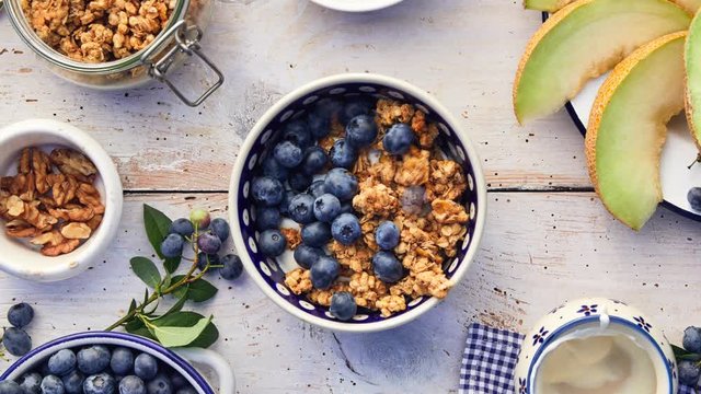 Granola with natural yogurt, fresh blueberries, nuts and honey, delicious breakfast or dessert, top view. Healthy eating concept. Stop motion animation.
