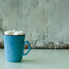 hot chocolate with marshmallows in a blue mug on a wooden table, square, copy space