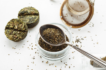 Dry green tea in a metal spoon with compressed tea near on a white background, top view, closeup shot