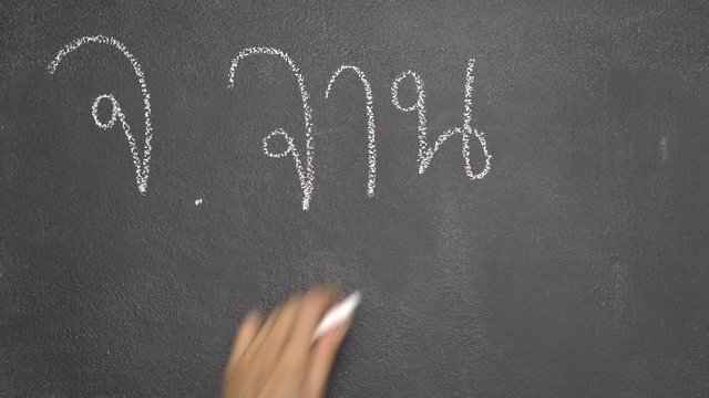 Woman's hand writing Thai letter "จ" with white chalk on blackboard