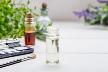 Small bottle with liquid in it and other vintage bottles, makeup items on a white wooden table