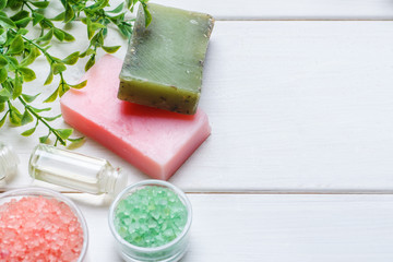 Handmade soap, sea salt, few glass vials with cosmetic oil, green plant branch on a white wooden table, text space