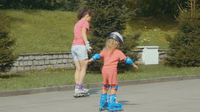  Family, young mother and daughter ride in a roller-skating park. A little girl and young woman in a helmet and defense skates on roller skates. The child rolls on the rollers in the park.  