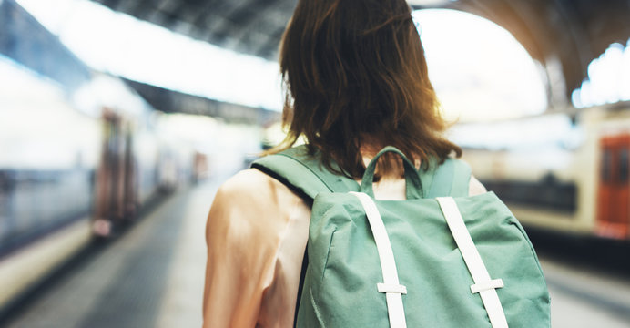 Enjoying travel. Young woman waiting on station platform with backpack on background electric train. Tourist plan route of railway, railroad transport concept trip, hipster lifestyle, timetable