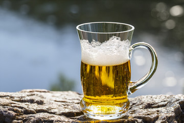 Mug of beer is stand on the rock above the river